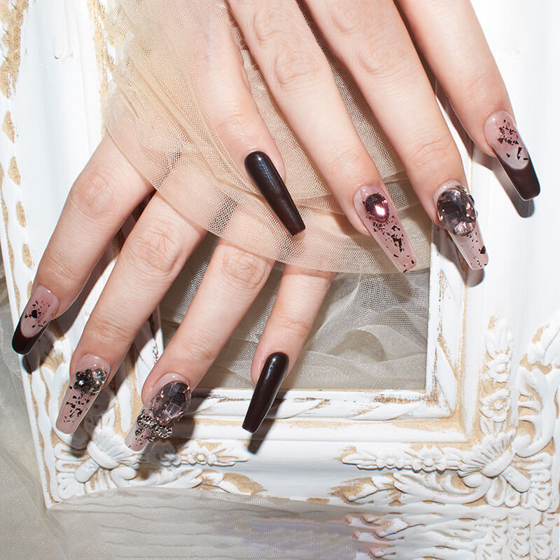 Close-up of hands with glamorous burgundy blush press-on nails featuring intricate designs and embellishments.