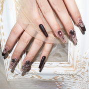 Close-up of hands with glamorous burgundy blush press-on nails featuring intricate designs and embellishments.
