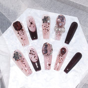 Set of burgundy blush press-on nails arranged on a white background, featuring various intricate designs and embellishments