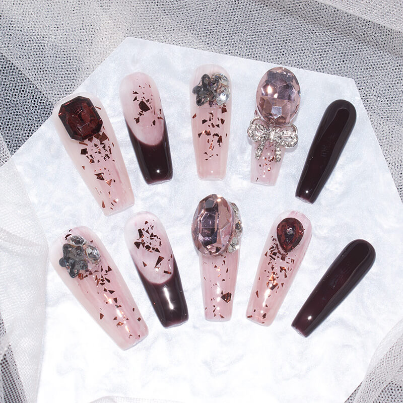 Set of burgundy blush press-on nails arranged on a white background, featuring various intricate designs and embellishments