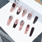 Detailed view of burgundy blush press-on nails with unique designs and sparkling accents, displayed on a white surface