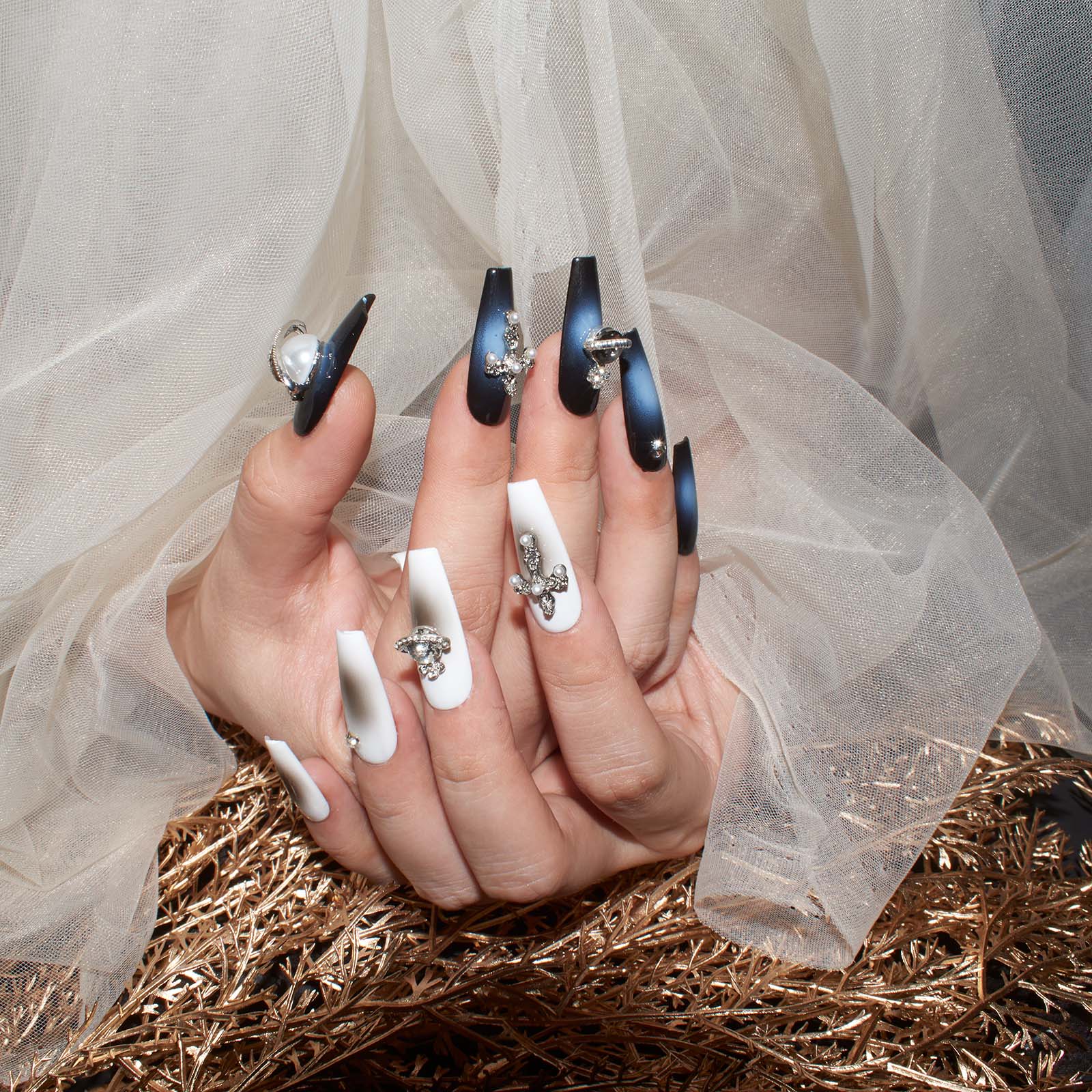 Mix of white and navy coffin-shaped press-on nails with 3D crosses, pearls, and rhinestones against sheer fabric