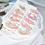 Pink candy matte press-on nails with 3D pearl and butterfly accents, elegantly arranged on a lace doily.