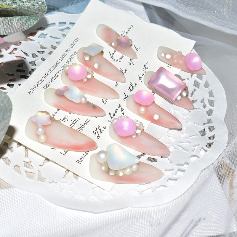Pink candy matte press-on nails with 3D pearl and butterfly accents, elegantly arranged on a lace doily.