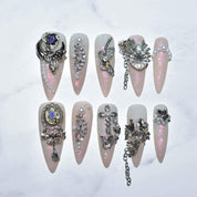 Set of Monoschic Prismatic Princess Press-On Nails arranged on a white marble surface, highlighting the intricate rhinestone, pearl, and charm designs on a light pink nude base.
