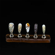 almond-shaped press-on nails with marble patterns, gold accents, and 3D embellishments on stands.