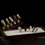 Press-on nails with marble patterns, gold accents, and 3D jewels on display stands against a black background.