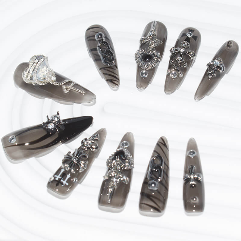 Long stiletto press-on nails in dark smoky hues with silver embellishments, including hearts, crosses, and chains