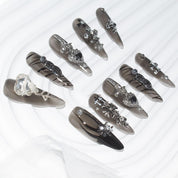 Set of stiletto-shaped press-on nails with black and silver designs, featuring 3D elements like hearts, crosses, and chains