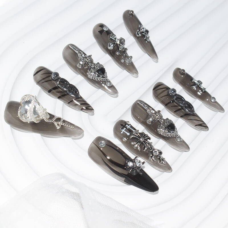 Set of stiletto-shaped press-on nails with black and silver designs, featuring 3D elements like hearts, crosses, and chains
