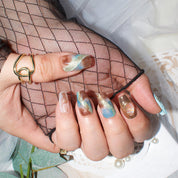 Close-up of hands displaying Monoschic Blue Gold Mirage Press-On Nails, showcasing an elegant marbled pattern with shimmering gold accents.