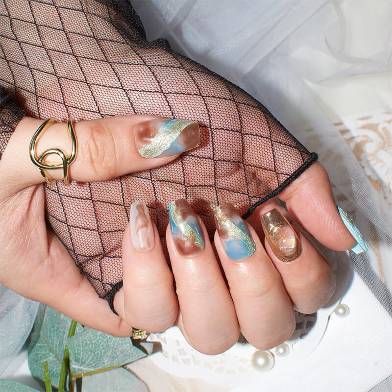 Close-up of hands displaying Monoschic Blue Gold Mirage Press-On Nails, showcasing an elegant marbled pattern with shimmering gold accents.