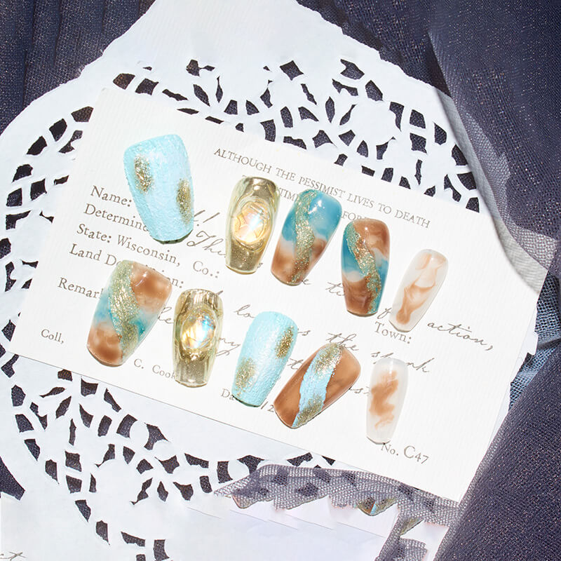 Set of Monoschic Blue Gold Mirage Press-On Nails arranged on a decorative card, highlighting the marbled design and gold shimmer.