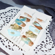Monoschic Blue Gold Mirage Press-On Nails displayed on a card, showcasing the blend of blue, brown, and gold tones with a marbled effect.