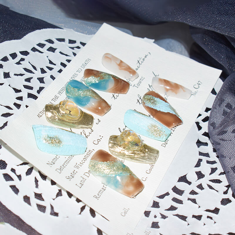 Monoschic Blue Gold Mirage Press-On Nails displayed on a card, showcasing the blend of blue, brown, and gold tones with a marbled effect.